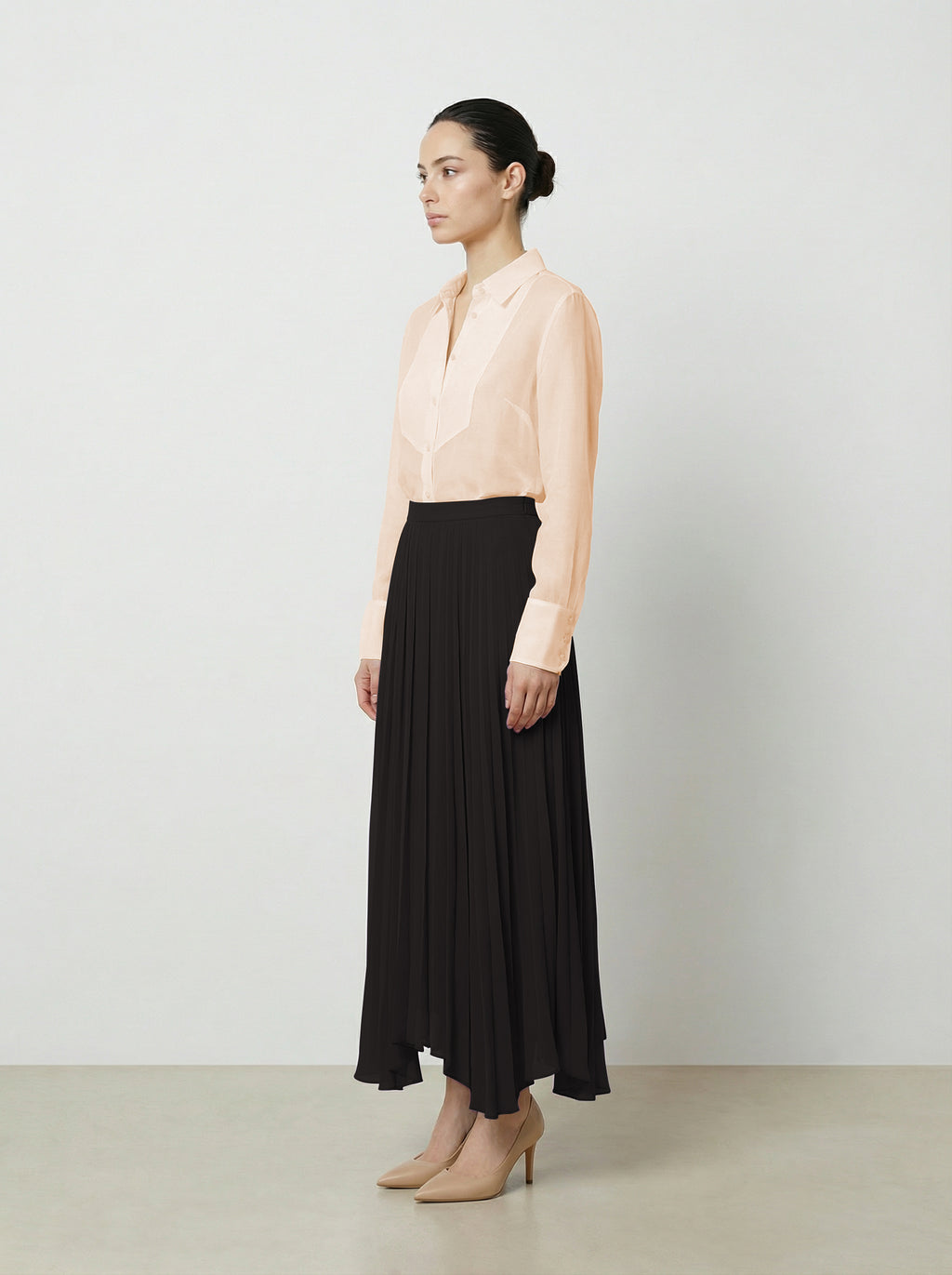 Woman wearing a light pink  organza blouse and black pleated skirt on a plain background