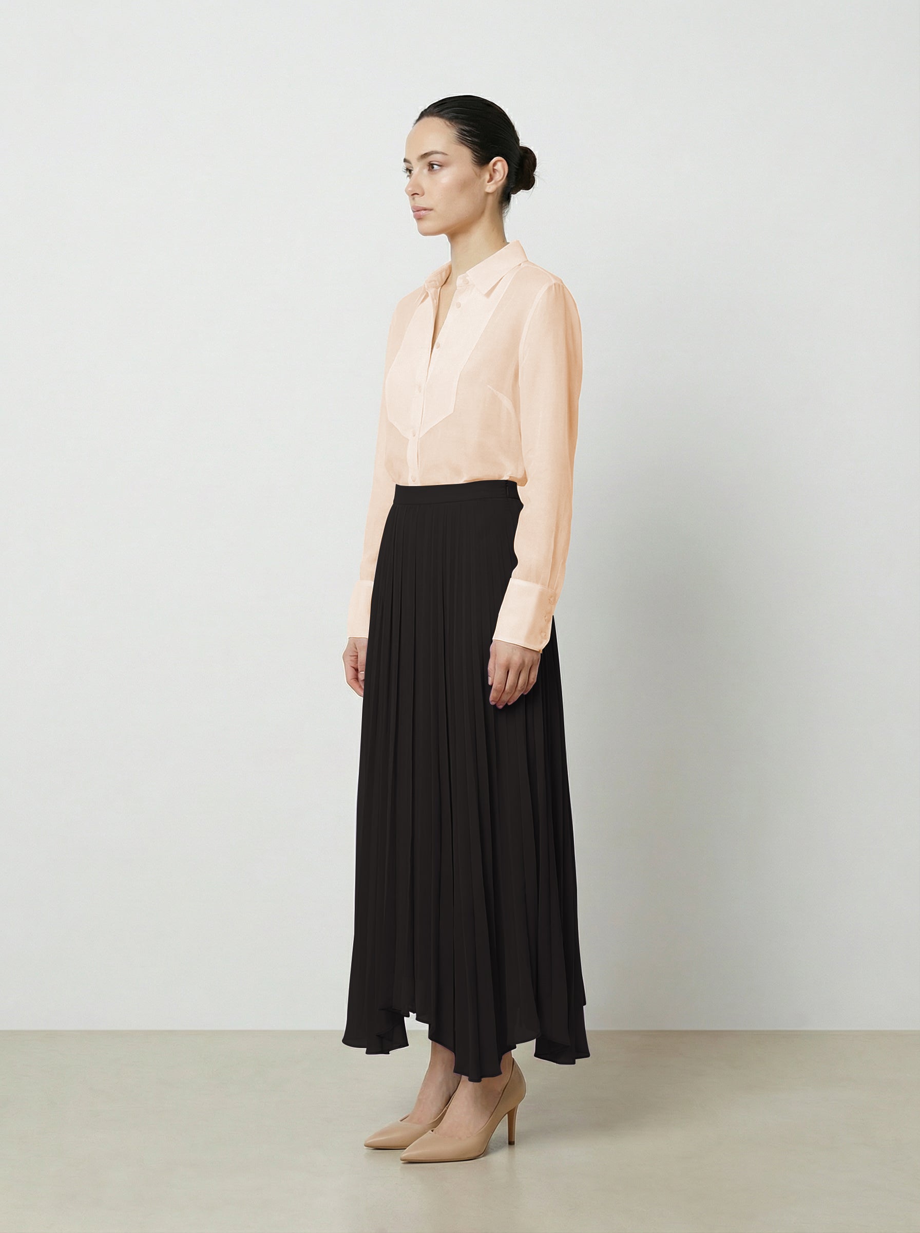 Woman wearing a light pink  organza blouse and black pleated skirt on a plain background