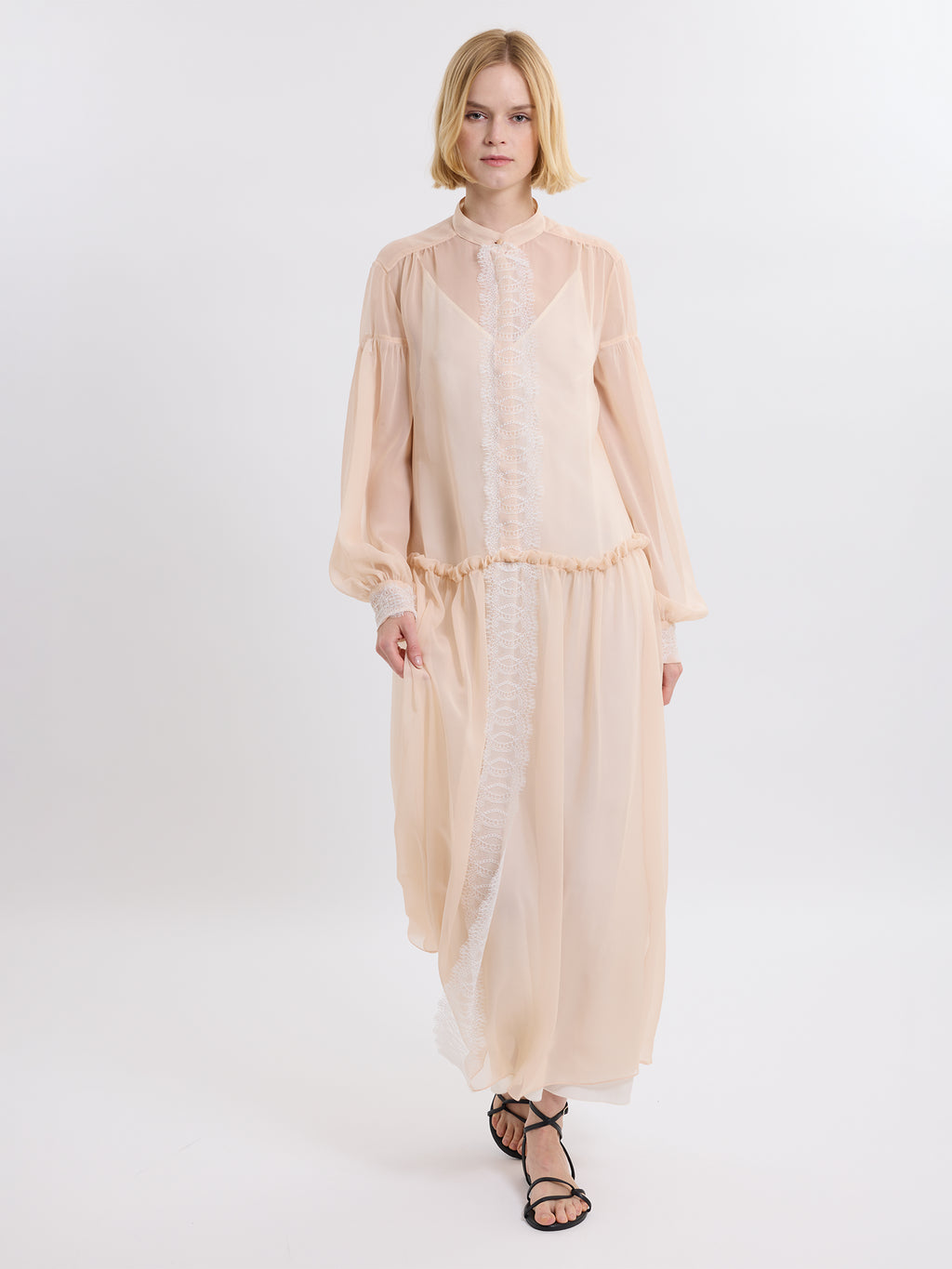 Model wearing a pink chiffon dress  with lace details on a white background