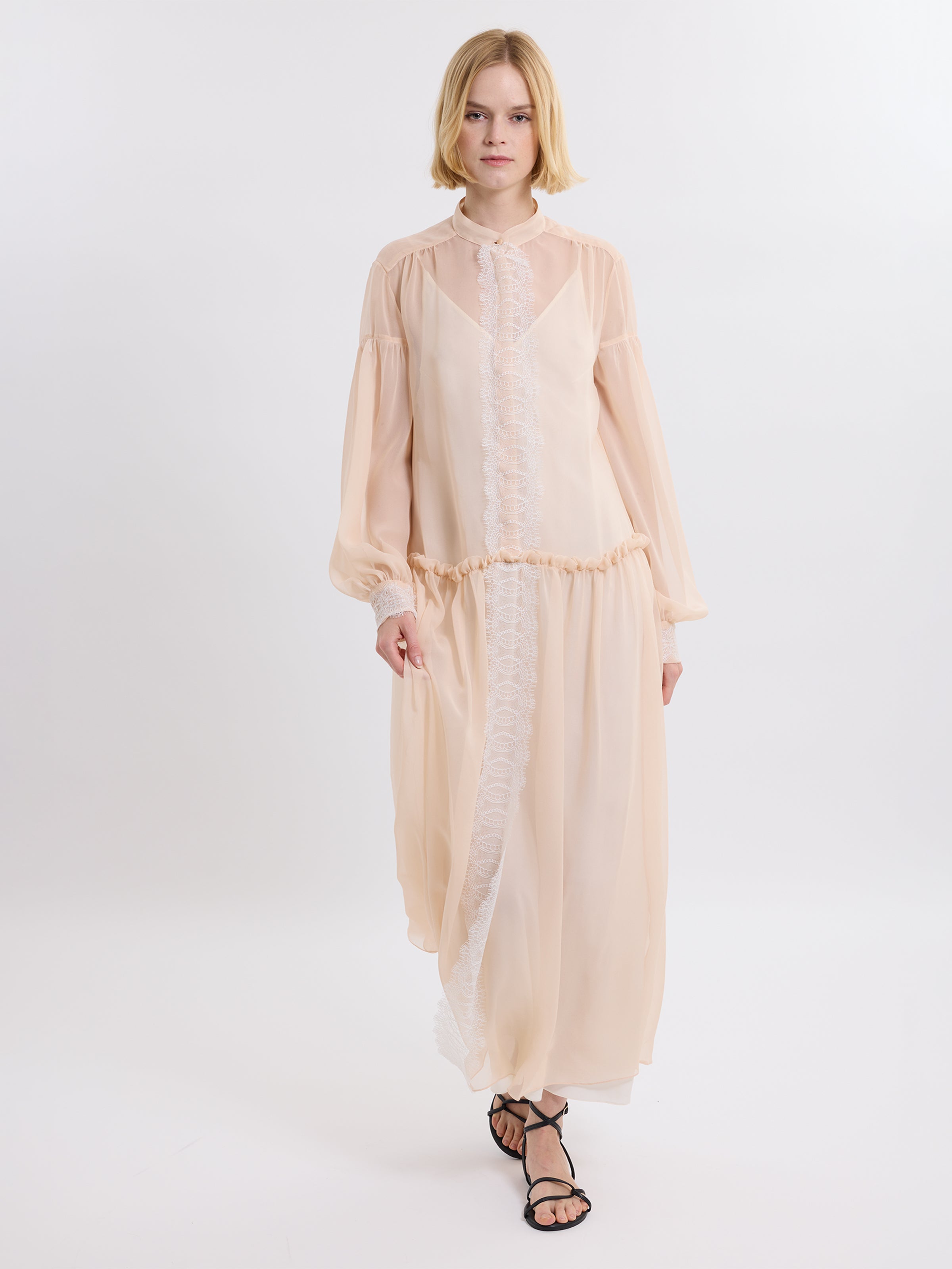 Model wearing a pink chiffon dress  with lace details on a white background