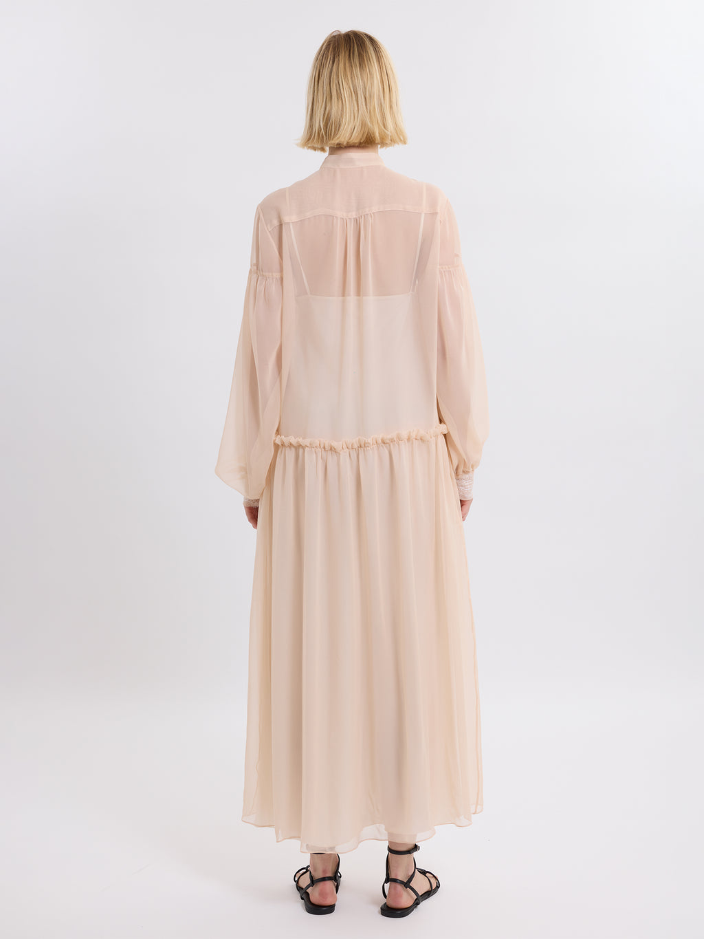 Woman wearing a pink chiffon dress with sheer sleeves on a white background