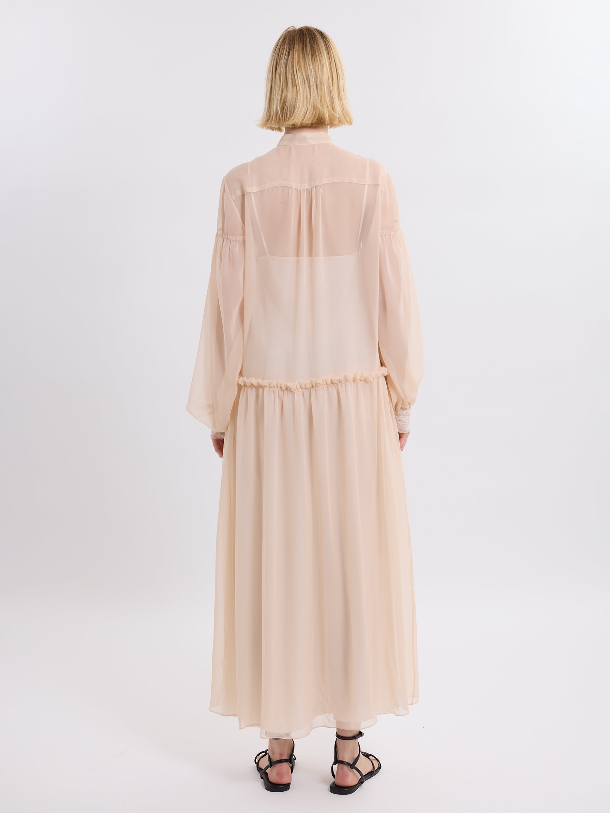 Woman wearing a pink chiffon dress with sheer sleeves on a white background