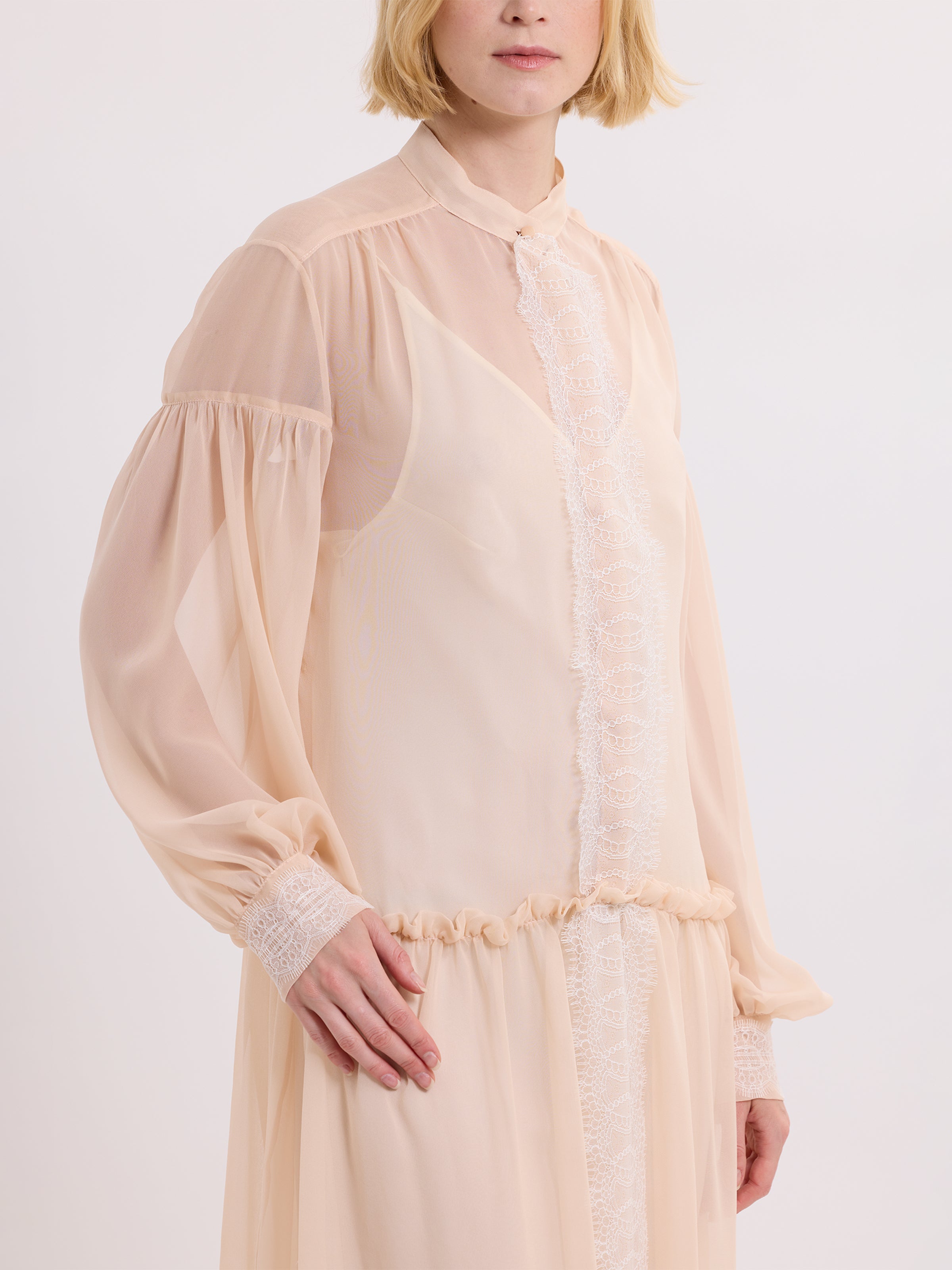 Woman wearing a light pink dress with sheer sleeves on a white background