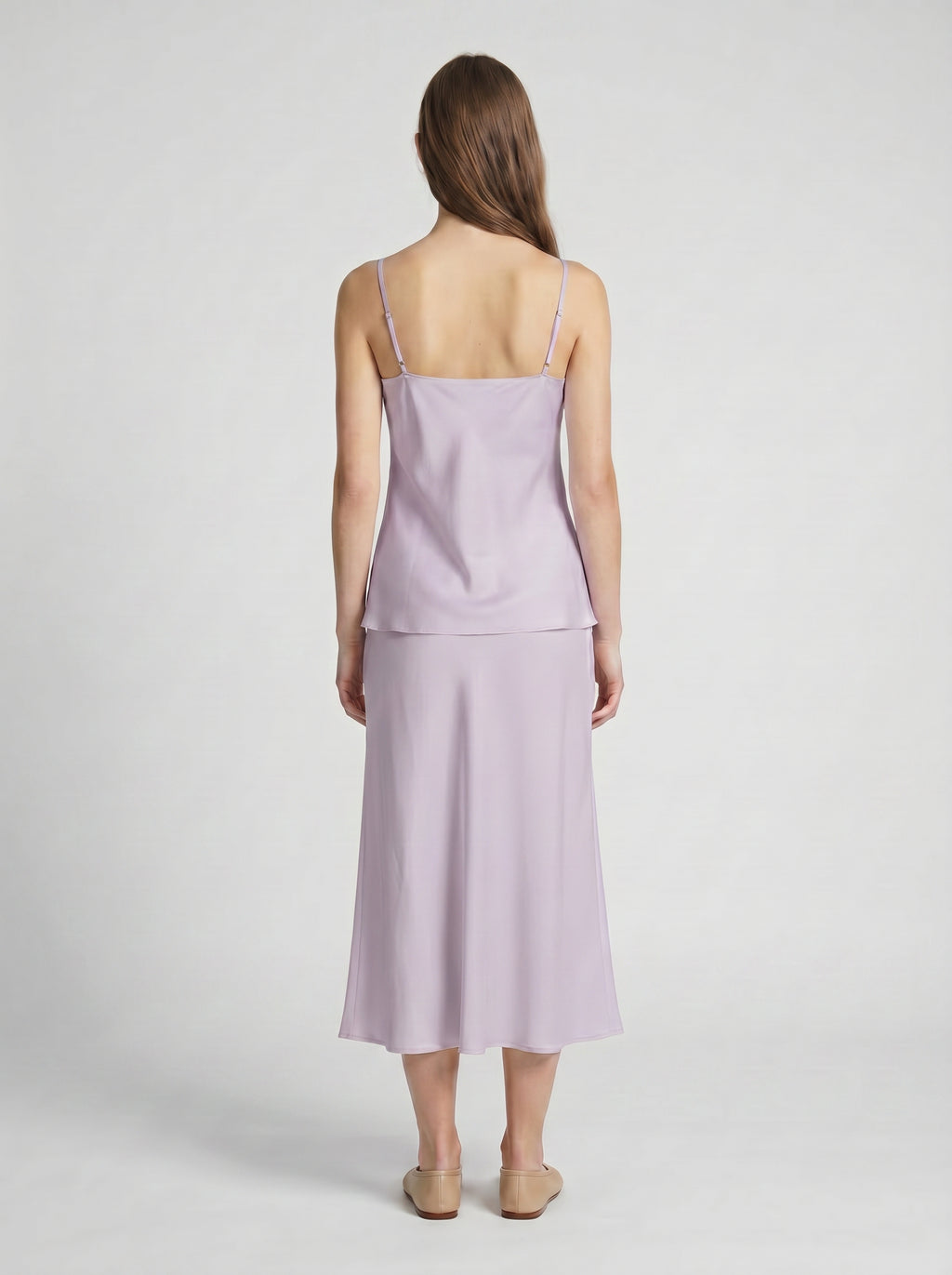 Woman wearing a light purple silk camisole top and half slip skirt on a white background