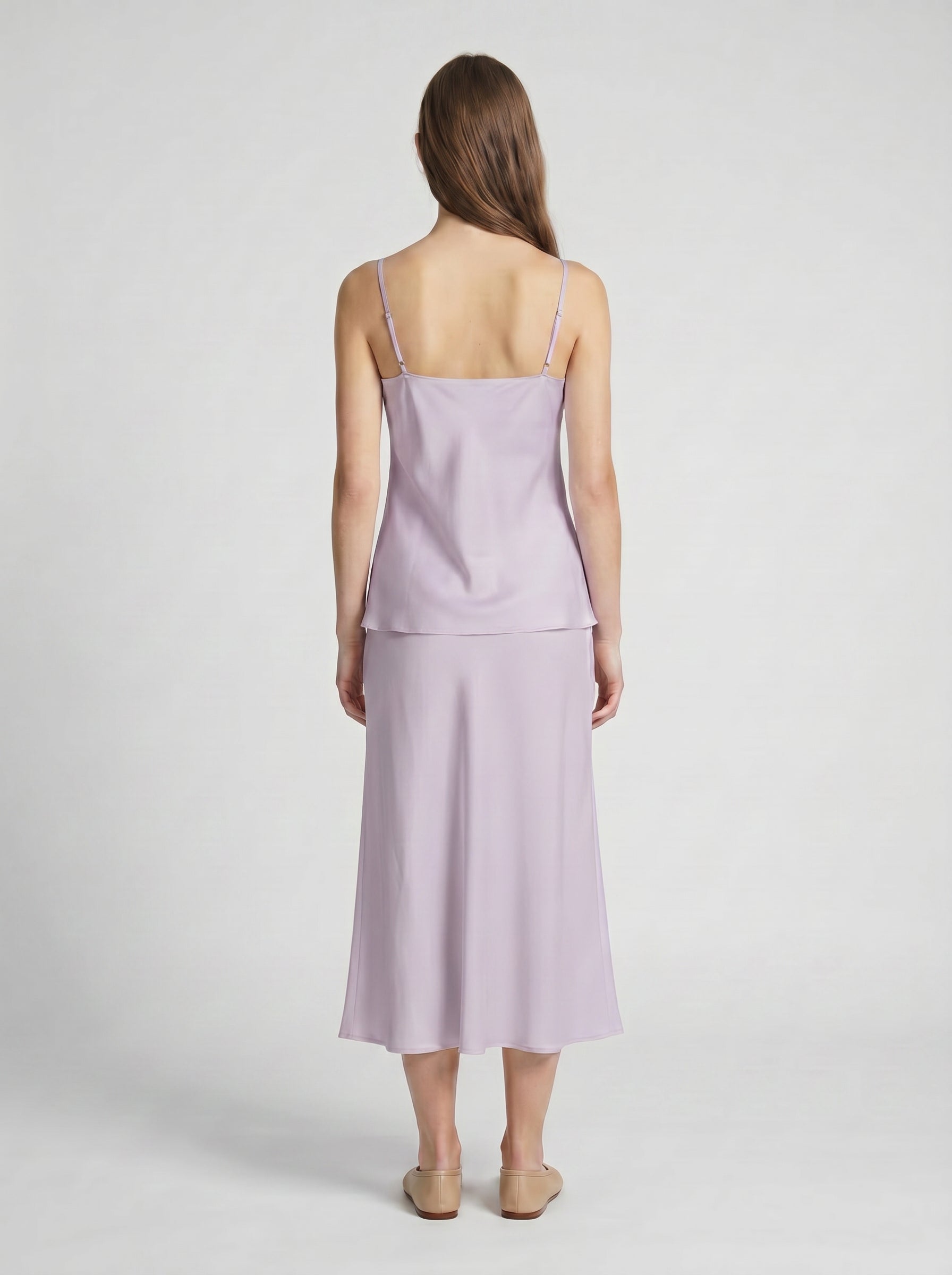 Woman wearing a light purple silk camisole top and half slip skirt on a white background
