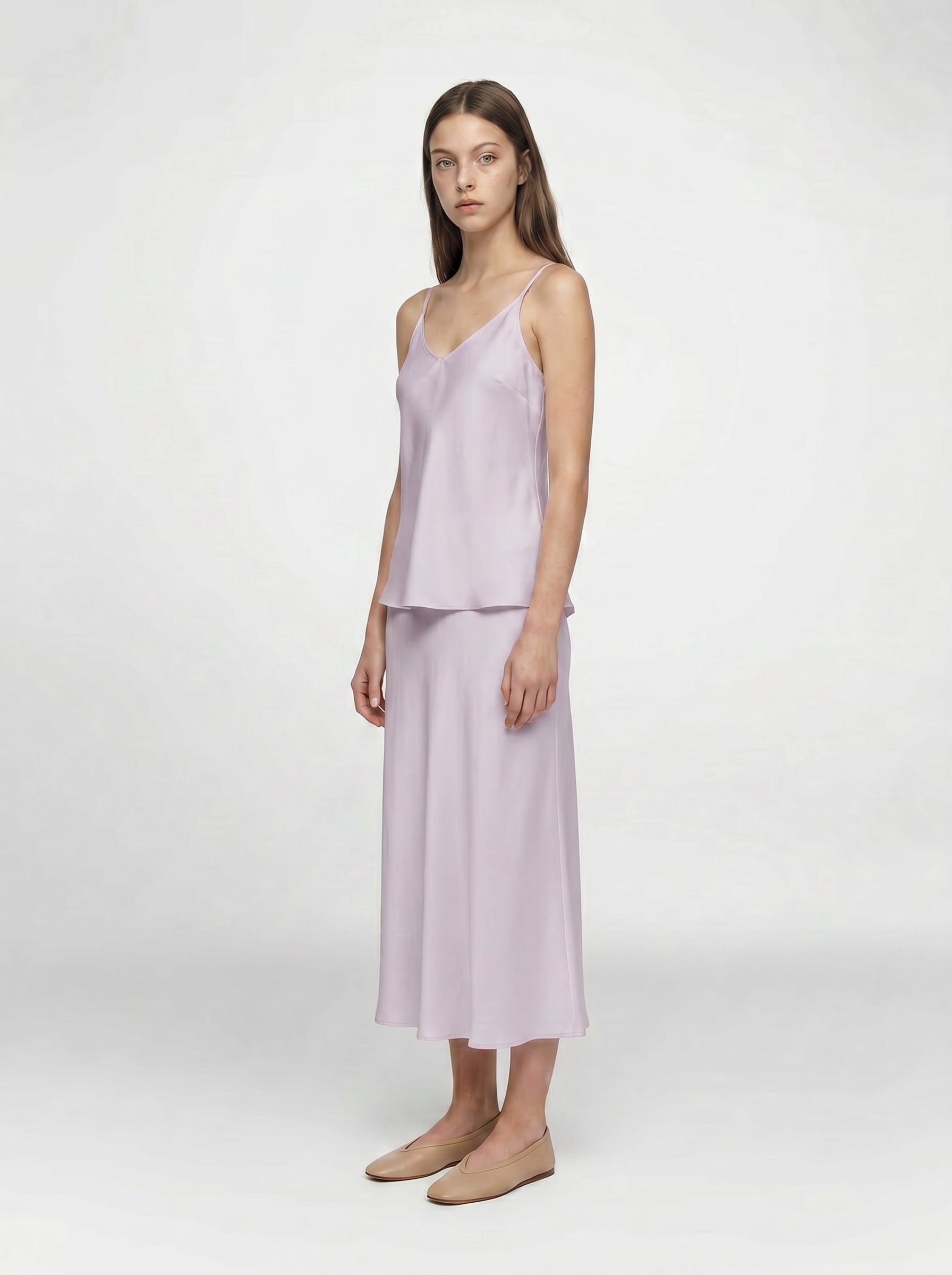 Woman wearing a light purple sleeveless top and s slip kirt set on a white background