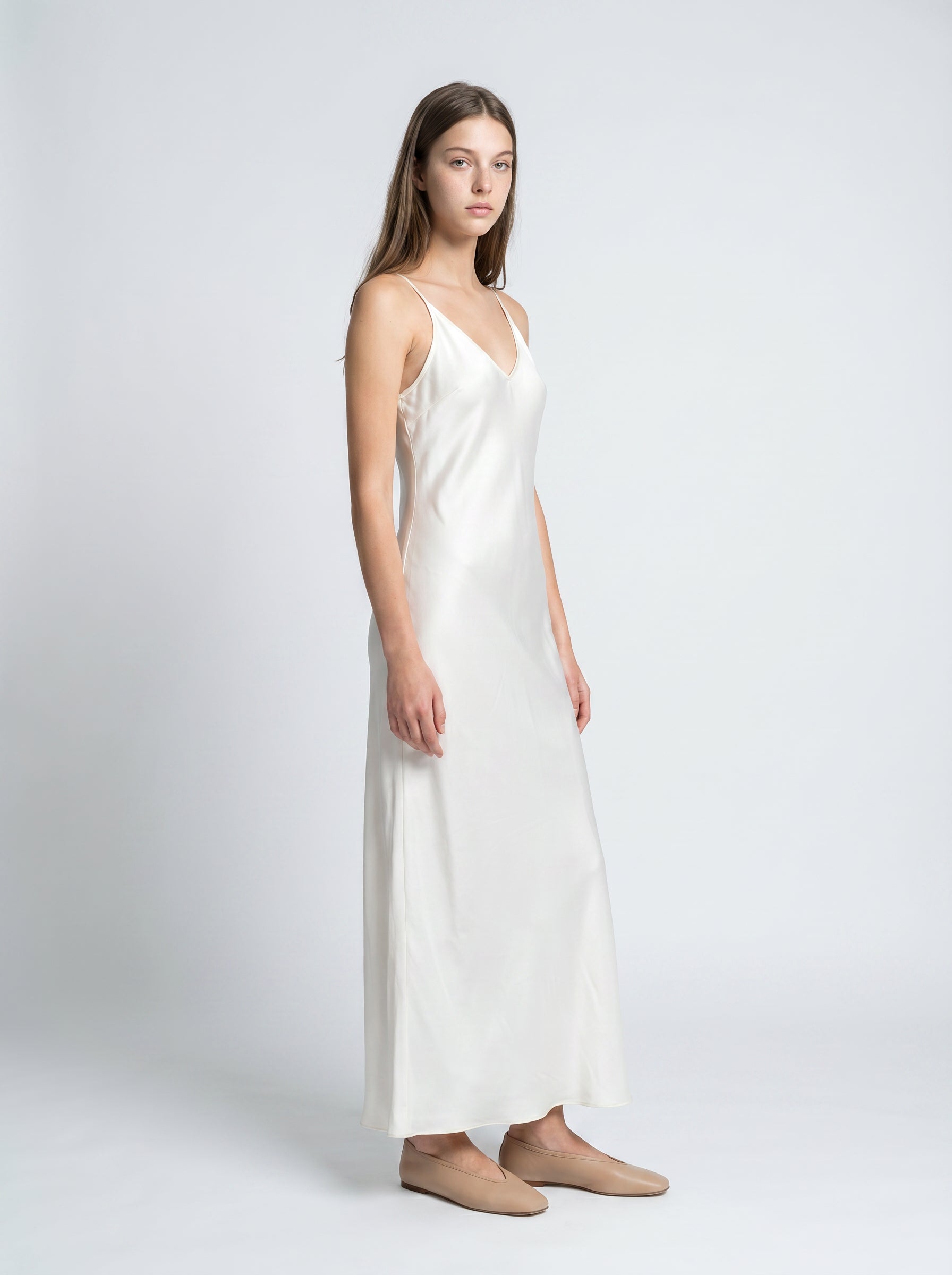 Woman wearing a white slip dress on a plain background