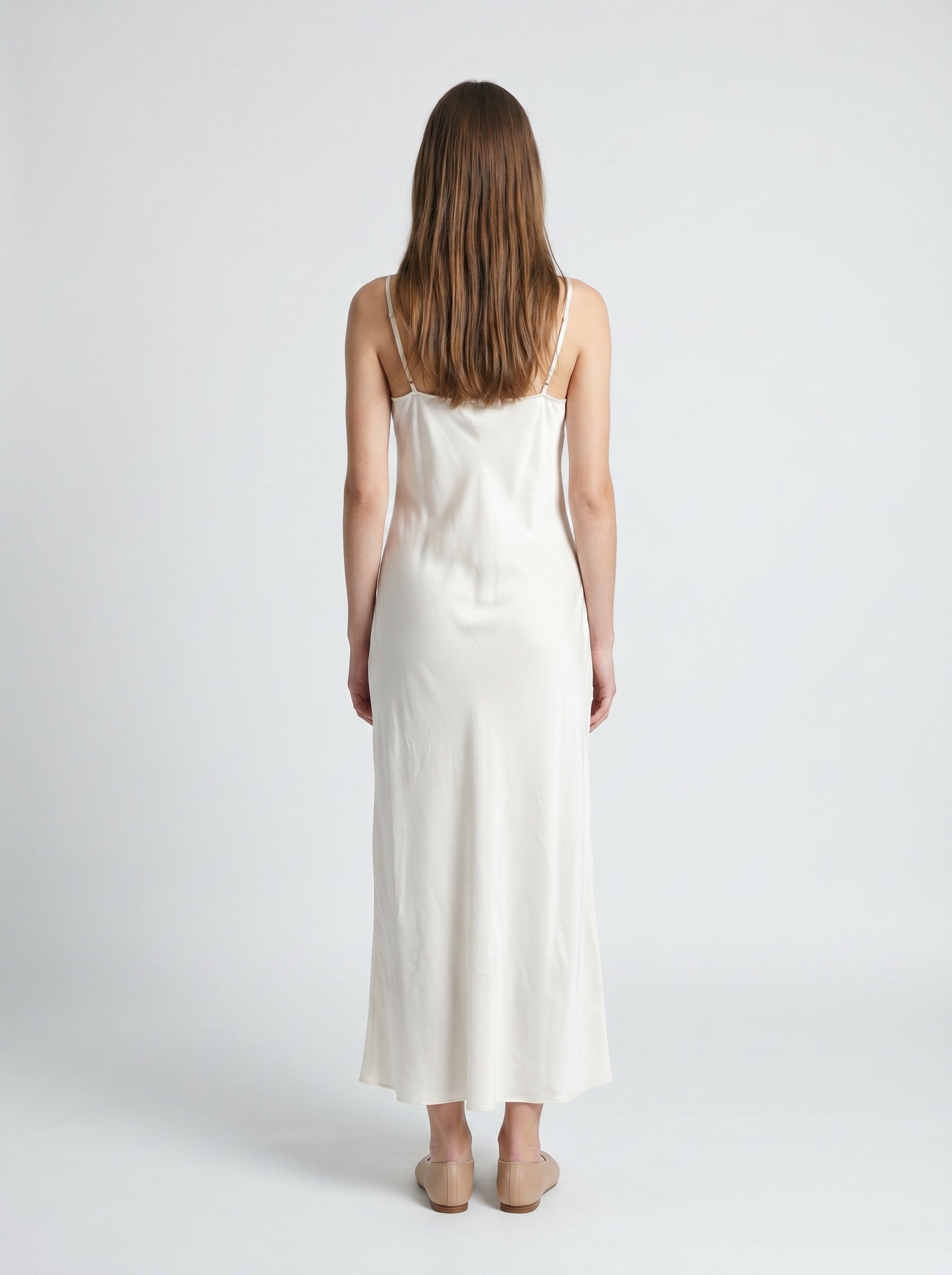 Woman wearing a white slip dress against a plain background