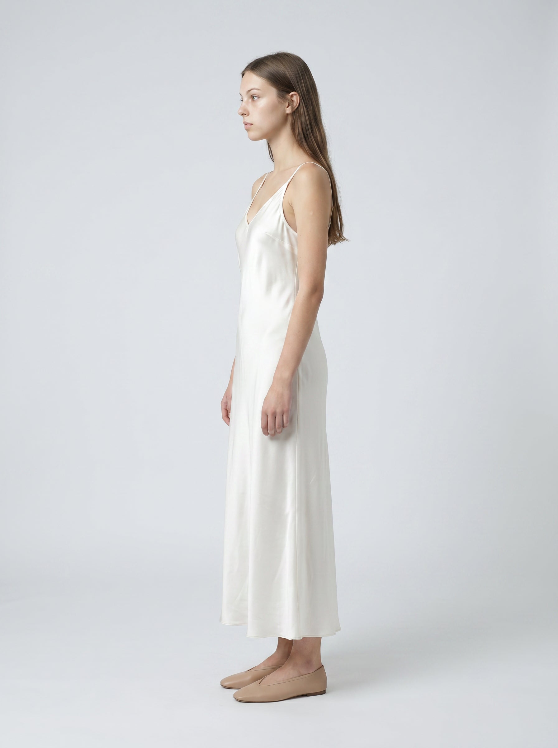 Woman wearing a white satin slip dress on a plain background