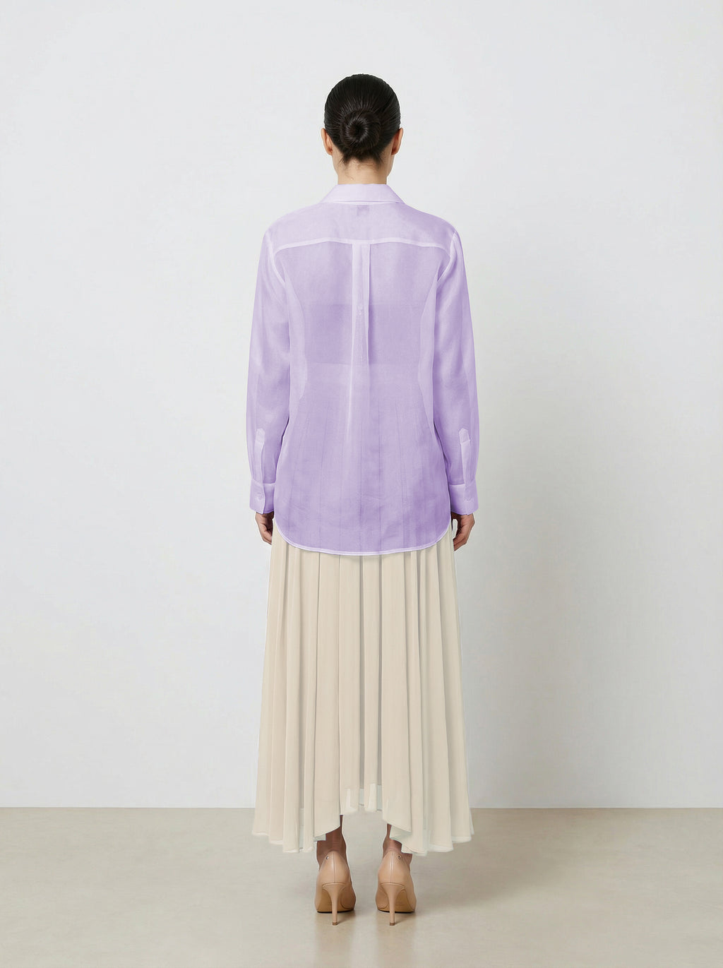 Woman wearing a light purple  translucent organza blouse and creme pleated skirt on a white background back view untucked shirt