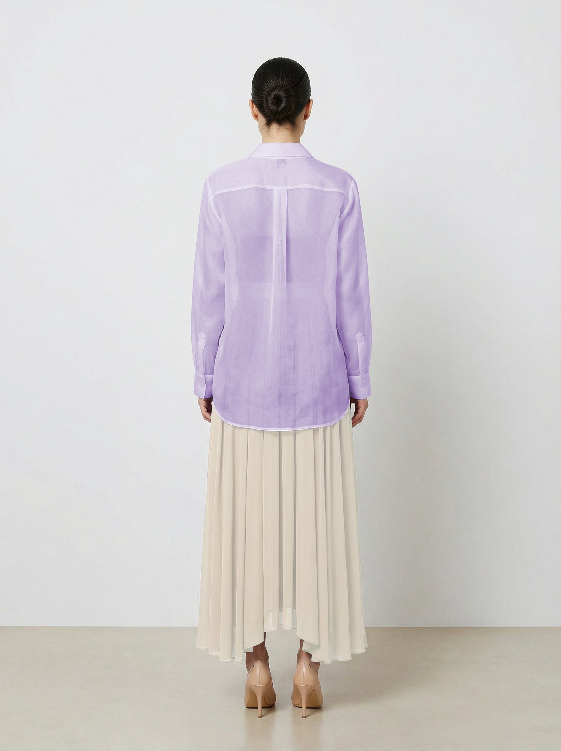 Woman wearing a light purple  translucent organza blouse and creme pleated skirt on a white background back view untucked shirt