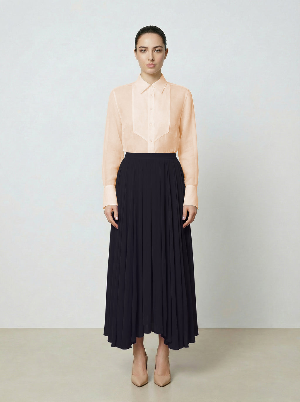 Woman wearing a light pink  organza blouse and black pleated skirt on a plain background