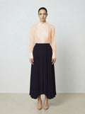 Woman wearing a light pink  organza blouse and black pleated skirt on a plain background