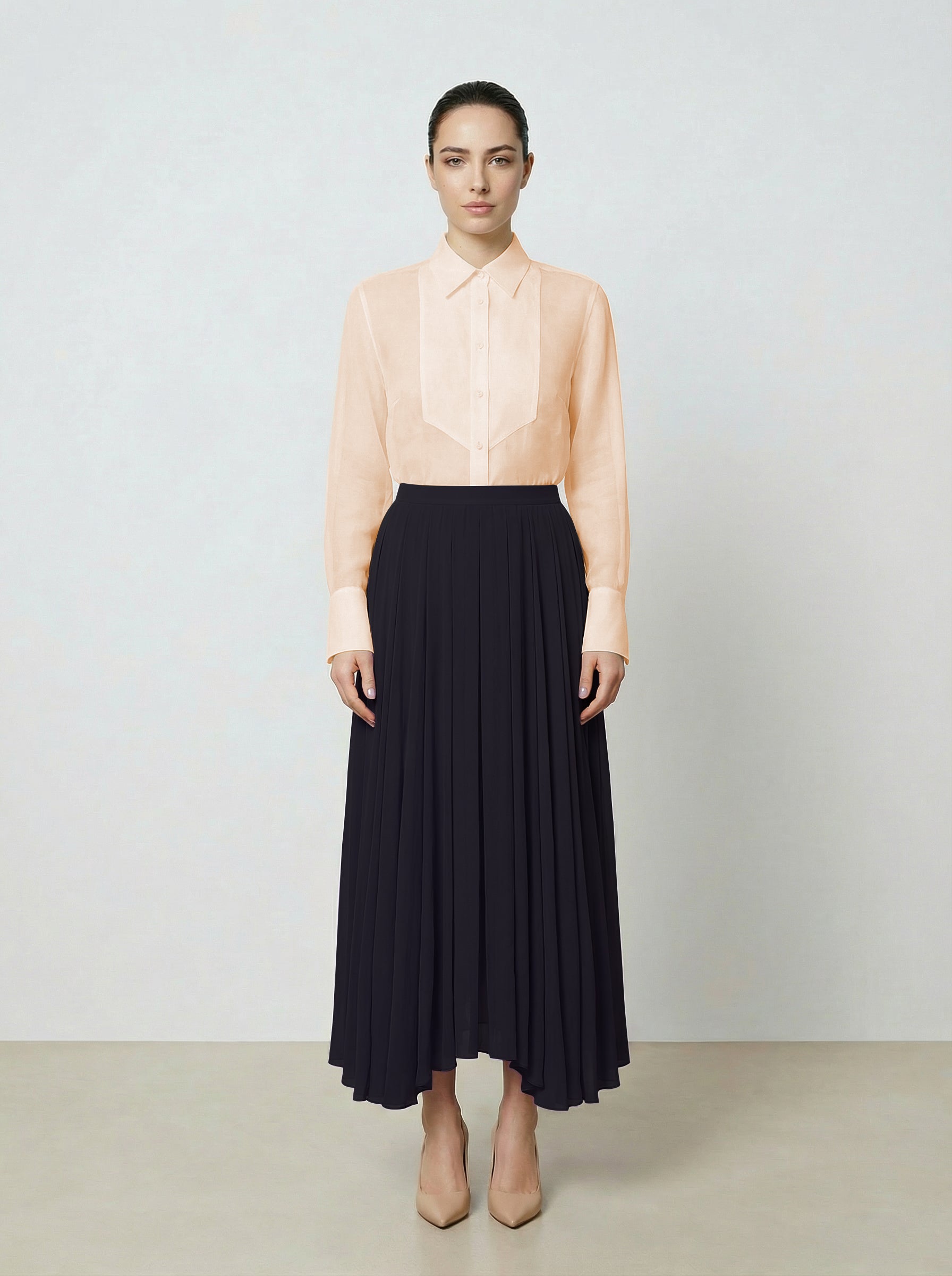 Woman wearing a light pink  organza blouse and black pleated skirt on a plain background