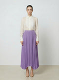 Woman wearing a creme colored  organza blouse and purple skirt on a plain background