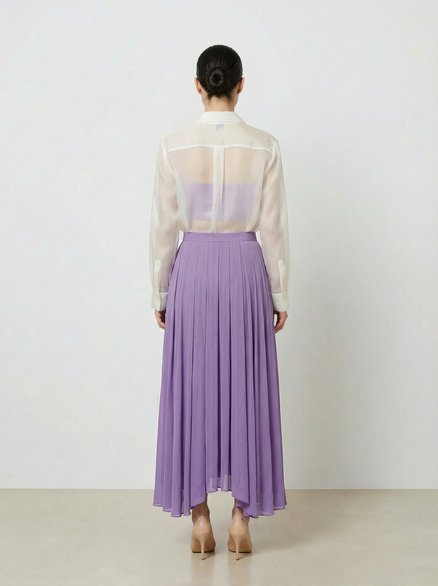 Person wearing a sheer white top and purple skirt on a plain background