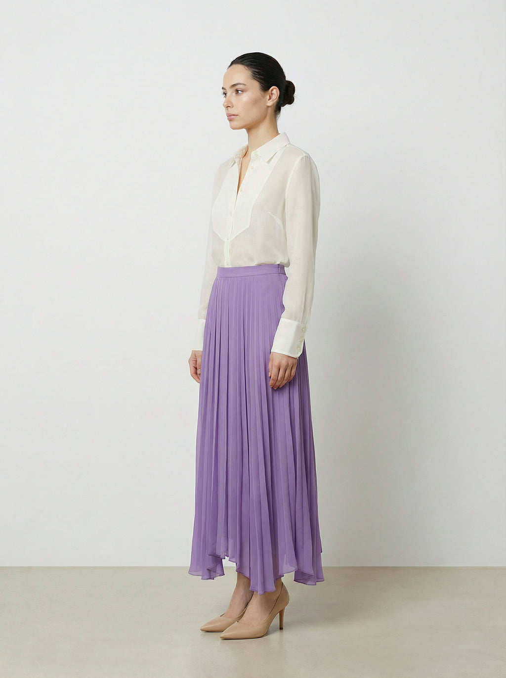Woman wearing a creme colored  organza blouse and purple skirt on a plain background