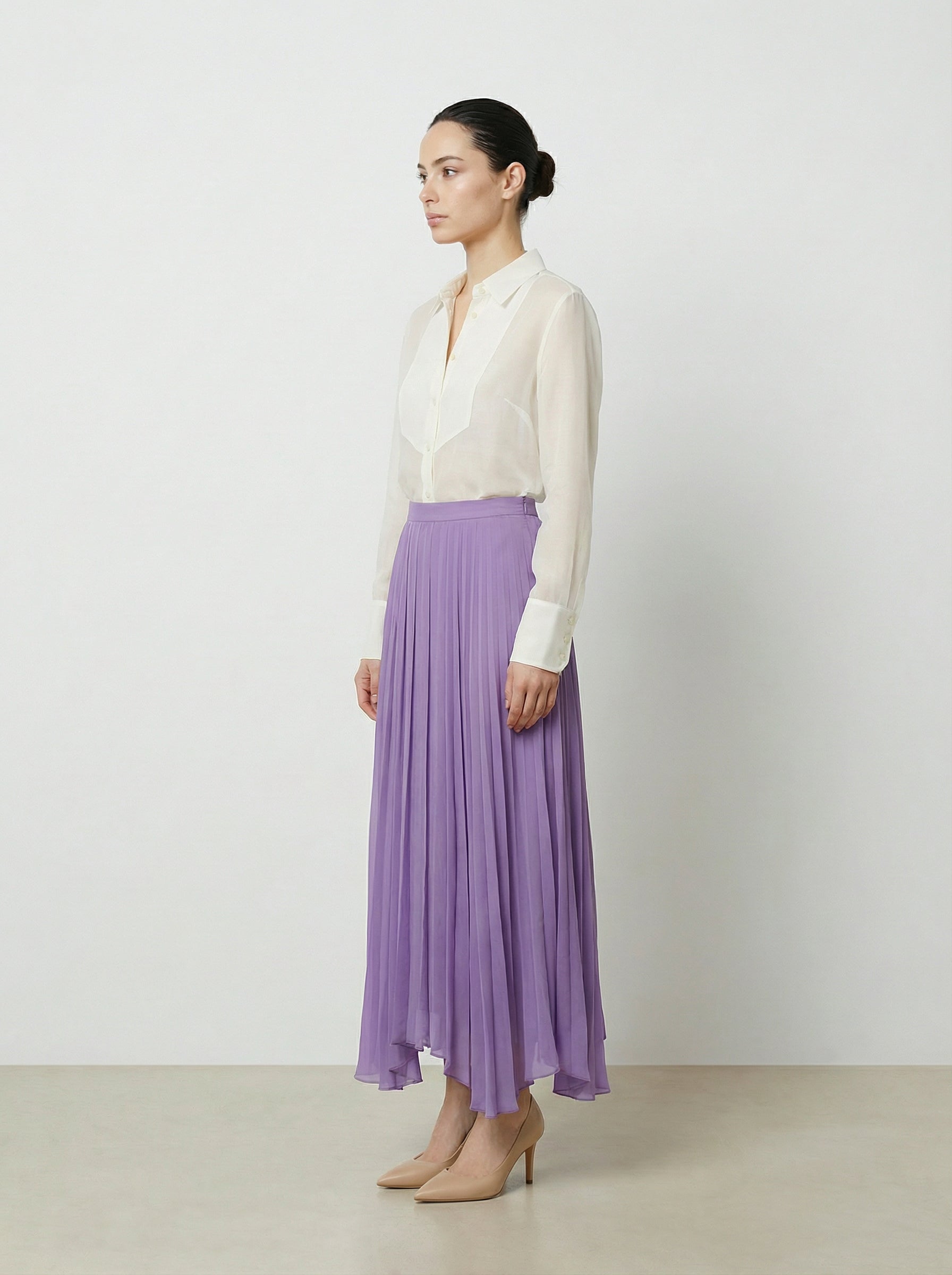 Woman wearing a creme colored  organza blouse and purple skirt on a plain background