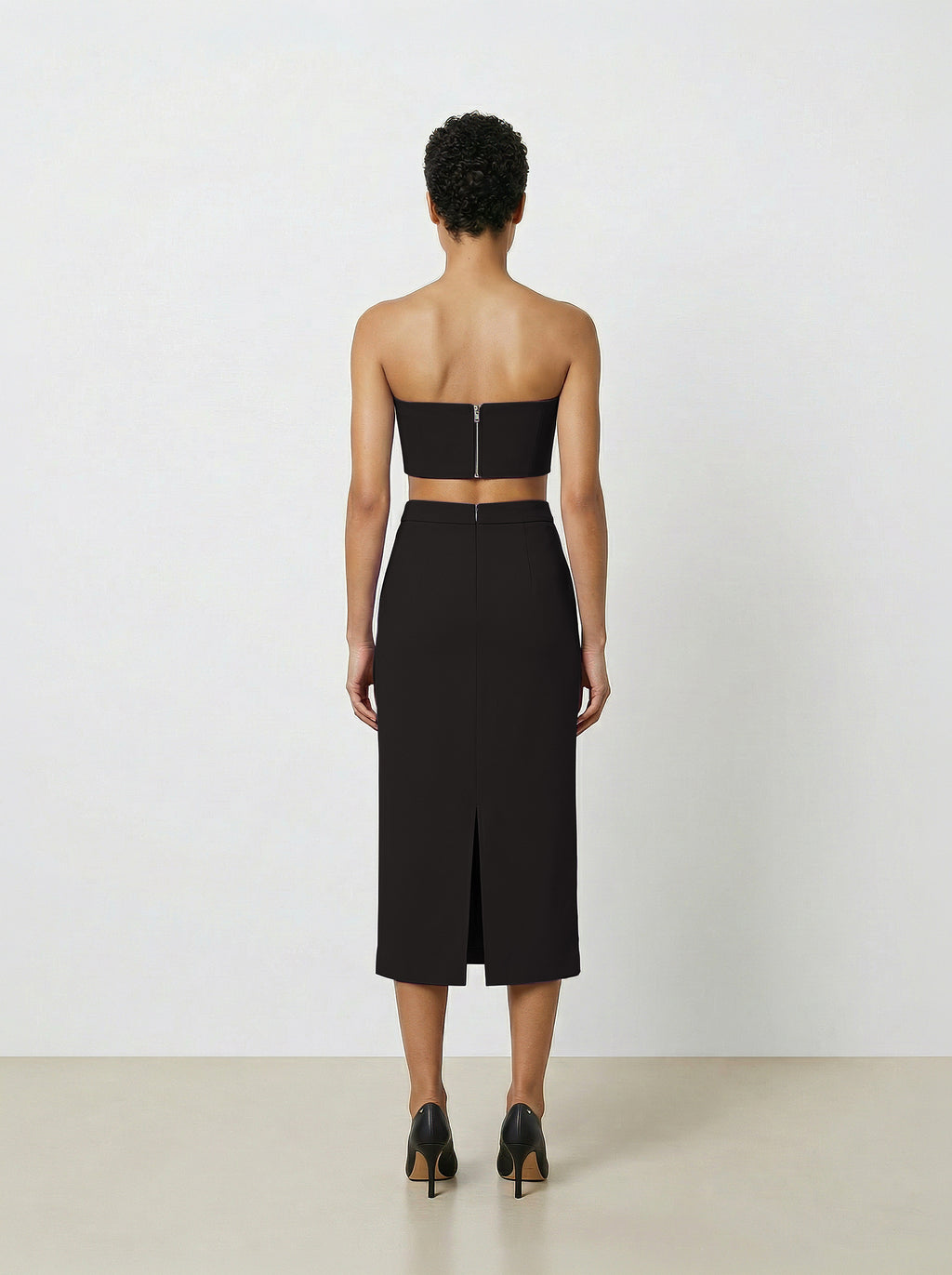 Woman wearing a black strapless top and pencil skirt on a white background back view
