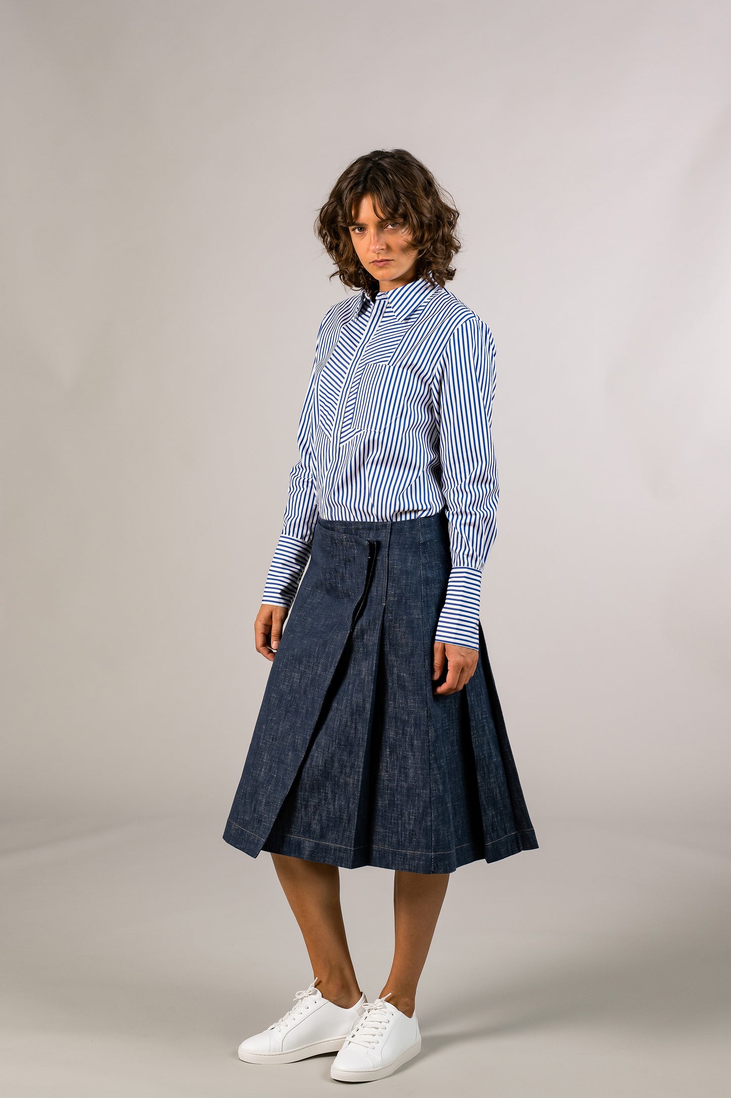 View of pleats on the womens knee high pleated wrap skirt, made with sustainable 100% cotton dark denim, hooked on side. Made in America.