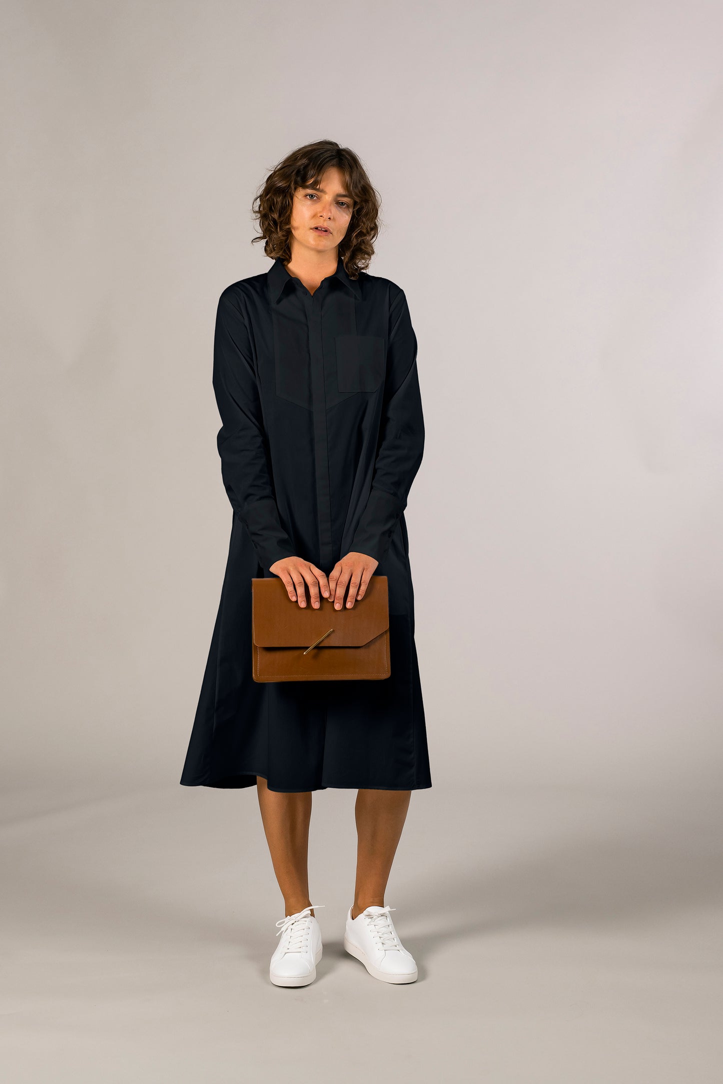 Womens navy tuxedo shirt dress, 100% sustainable cotton poplin from Italy, long sleeve, button down knee length. Ensembled with large brown leather clutch bag.