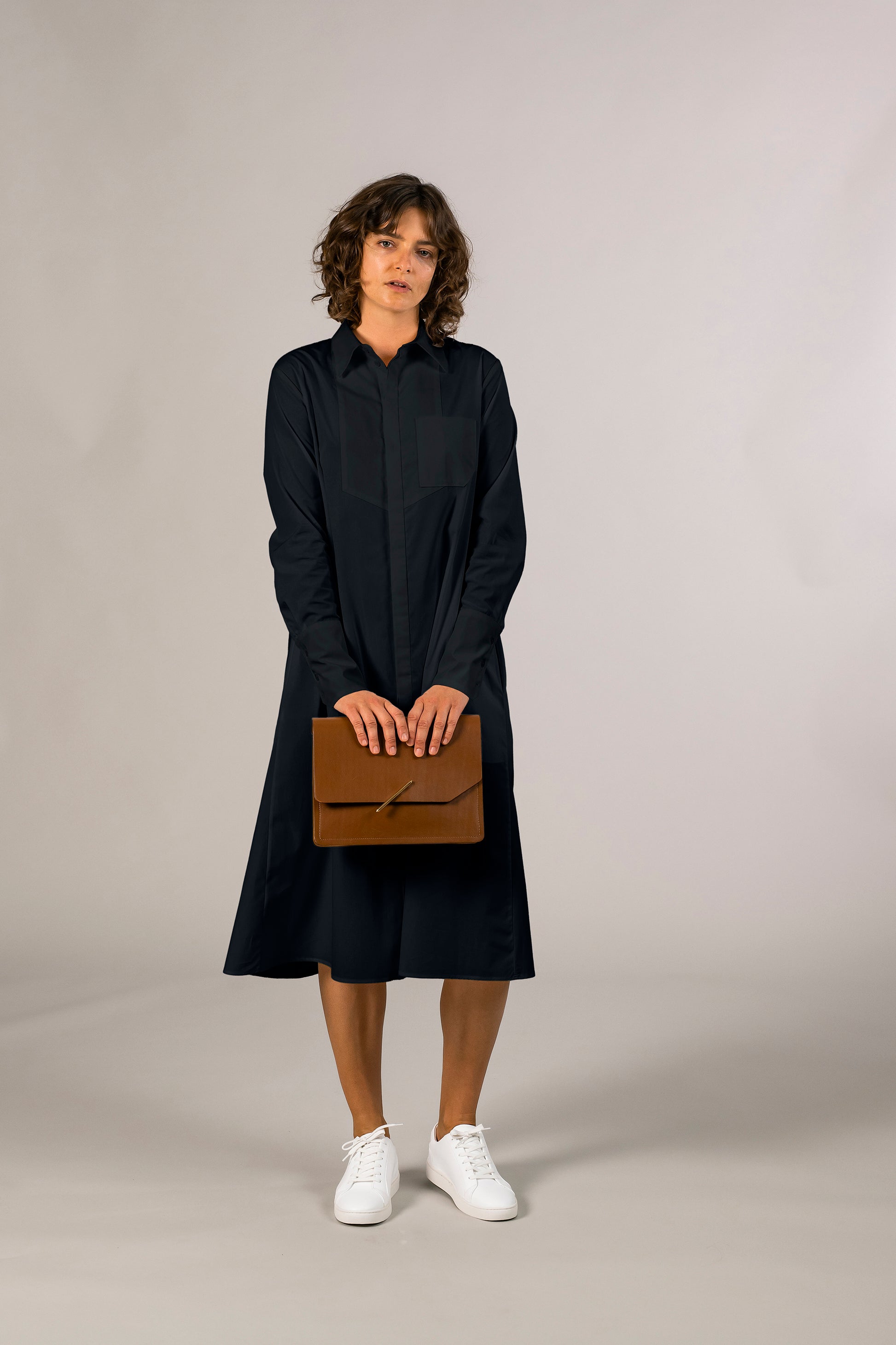 Womens navy tuxedo shirt dress, 100% sustainable cotton poplin from Italy, long sleeve, button down knee length. Ensembled with large brown leather clutch bag.